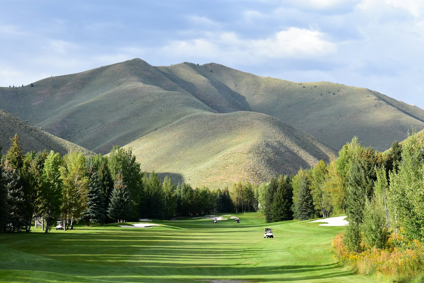 Golf carts parked on a fairway below rolling green mountains.