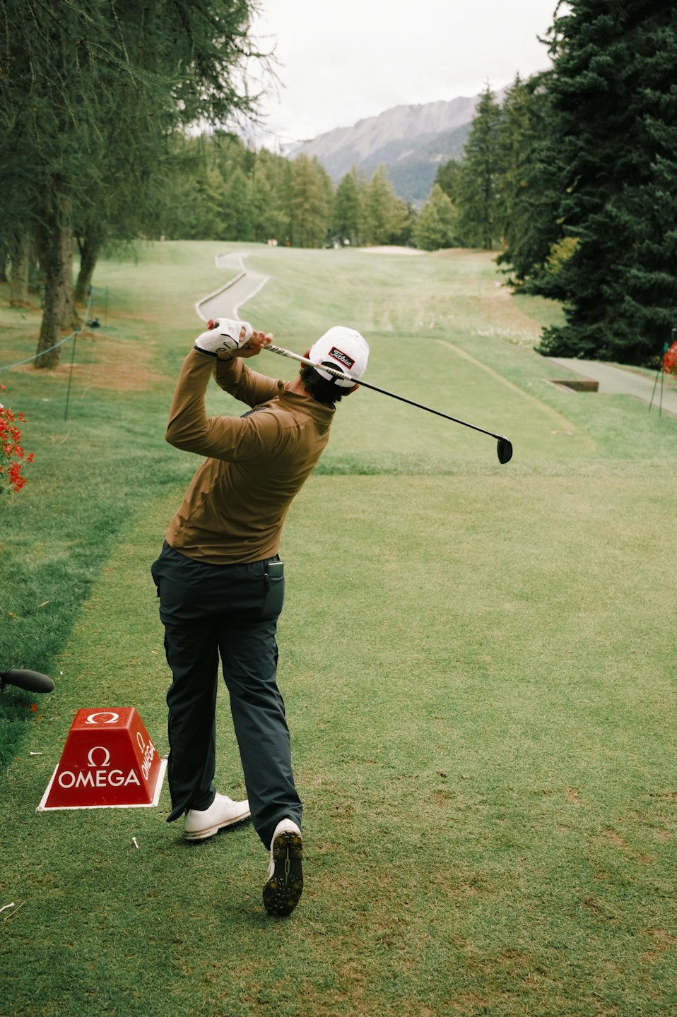 A golfer swings a club on a green course with mountains.