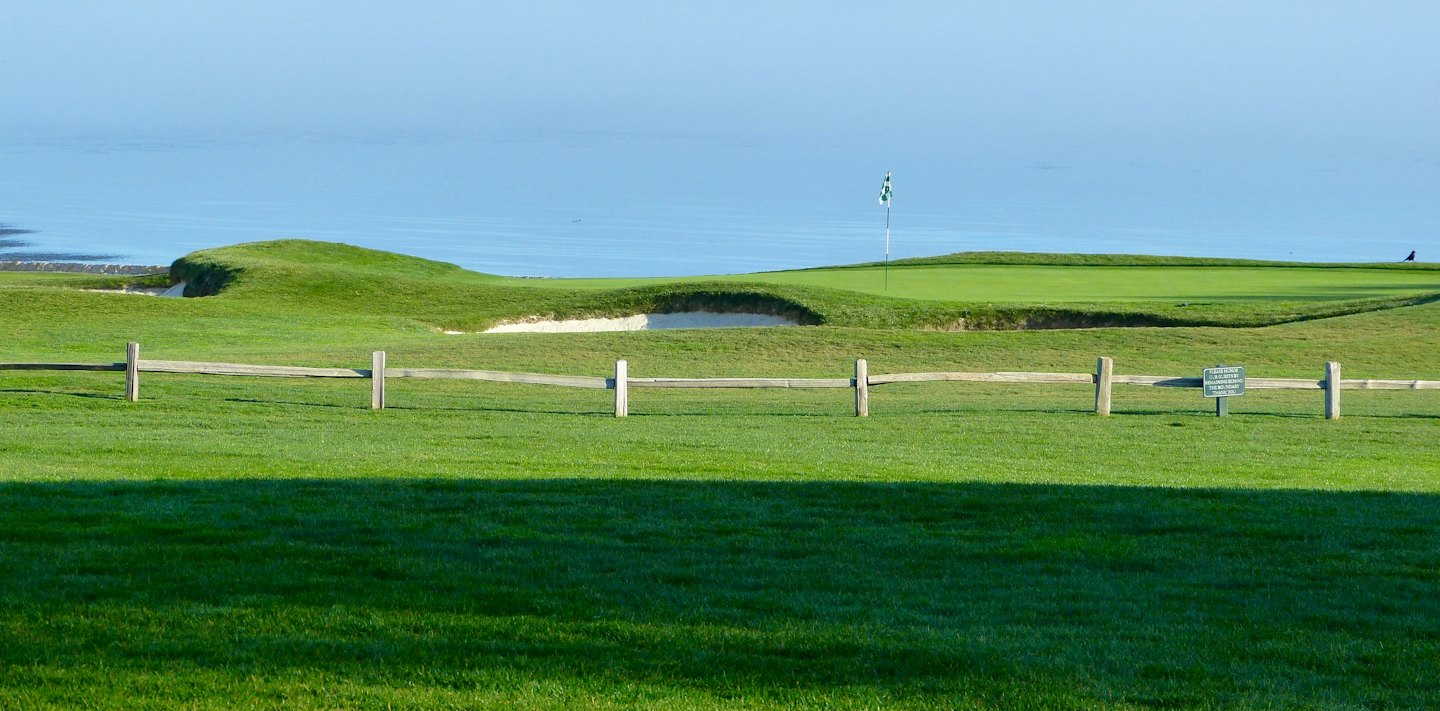 Wooden fence borders a scenic coastal golf green by the ocean.