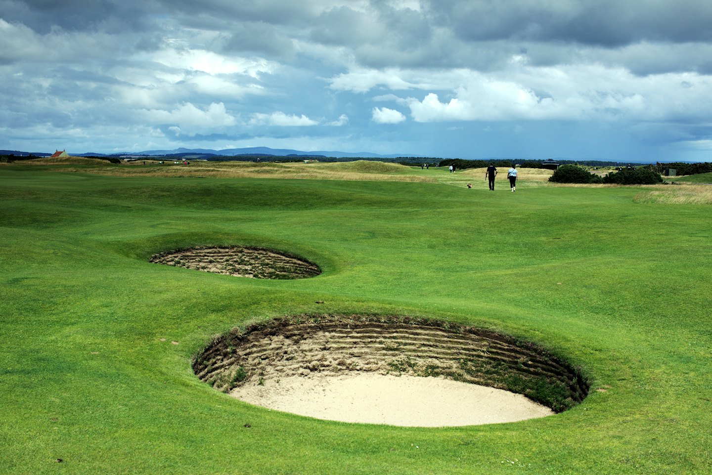 Golfers walking on a links course fairway near sandy bunkers.